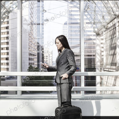 A businesswoman with a suitcase standing using a phone in a large open space under a… A businesswoman with a suitcase standing using a phone in a large open space under a…