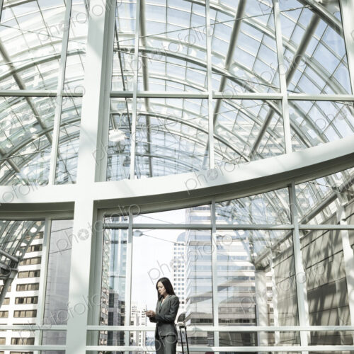 A businesswoman with a suitcase standing using a phone in a large open space under a… A businesswoman with a suitcase standing using a phone in a large open space under a…