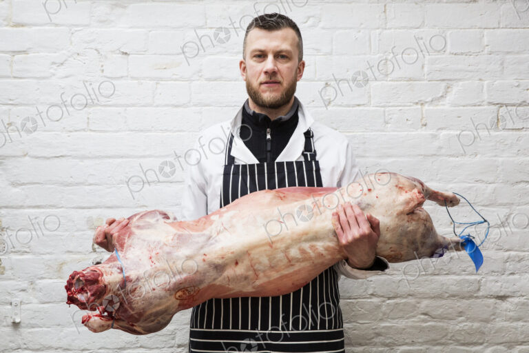 A butcher holding a complete prepared lamb meat carcass for cutting into smaller…