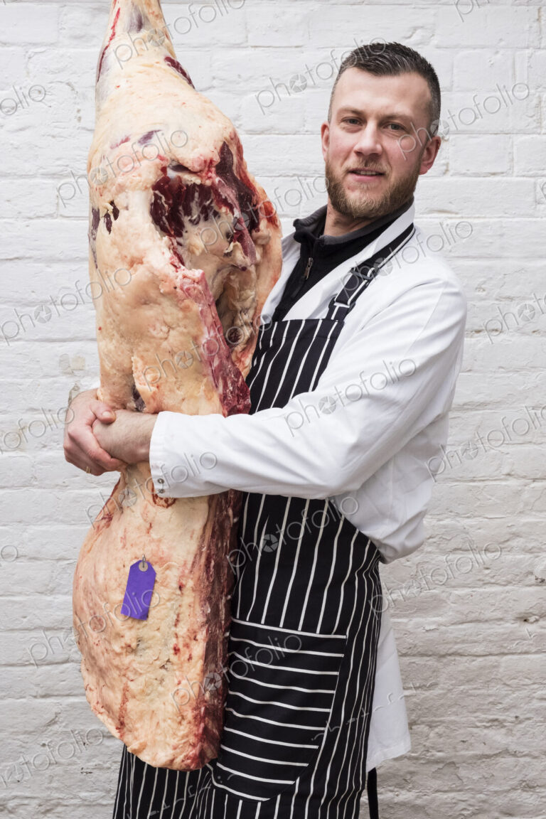 A butcher holding a complete prepared lamb meat carcass for cutting into smaller…