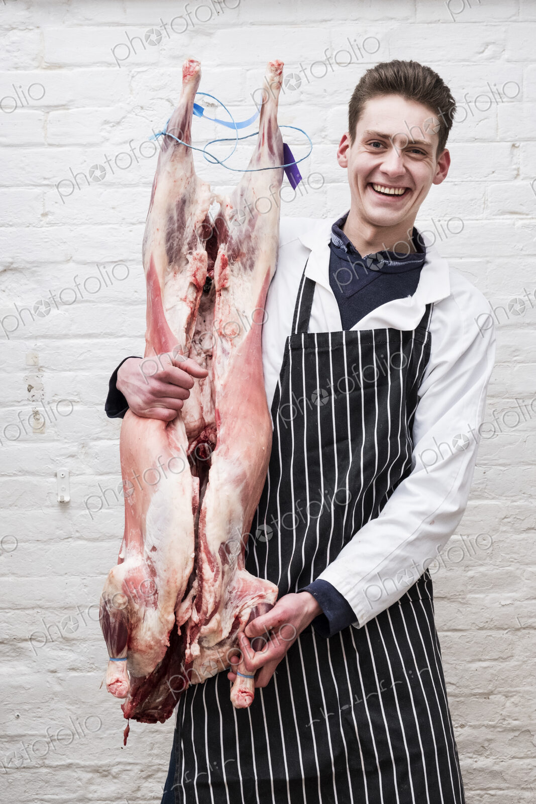 A butcher holding a complete prepared lamb meat carcass for cutting into smaller…