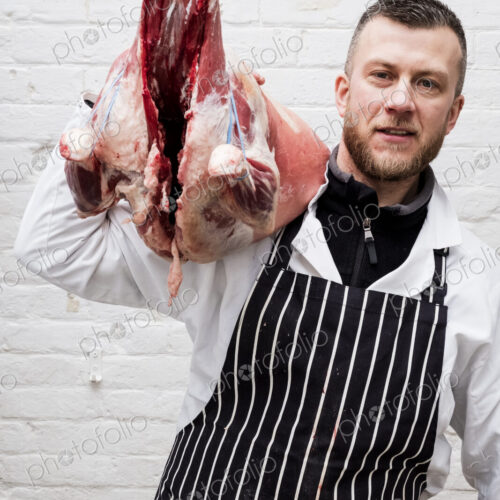A butcher holding a complete prepared lamb meat carcass for cutting into smaller…