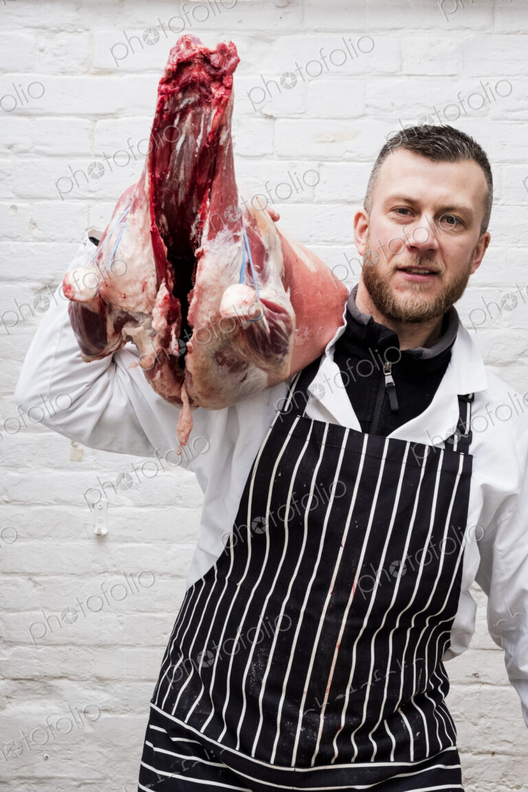 A butcher holding a complete prepared lamb meat carcass for cutting into smaller…