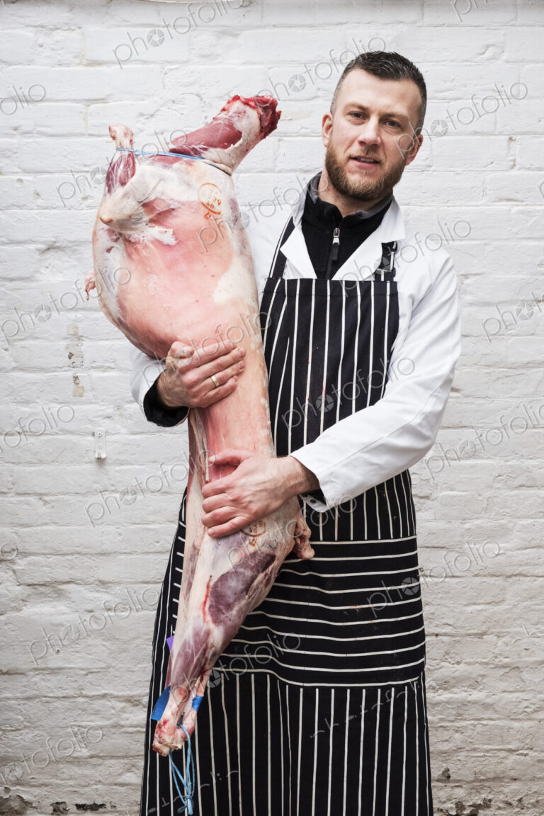A butcher holding a complete prepared lamb meat carcass for cutting into smaller…