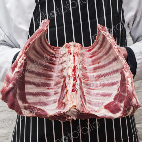 A butcher holding the ribs of a lamb carcass.
