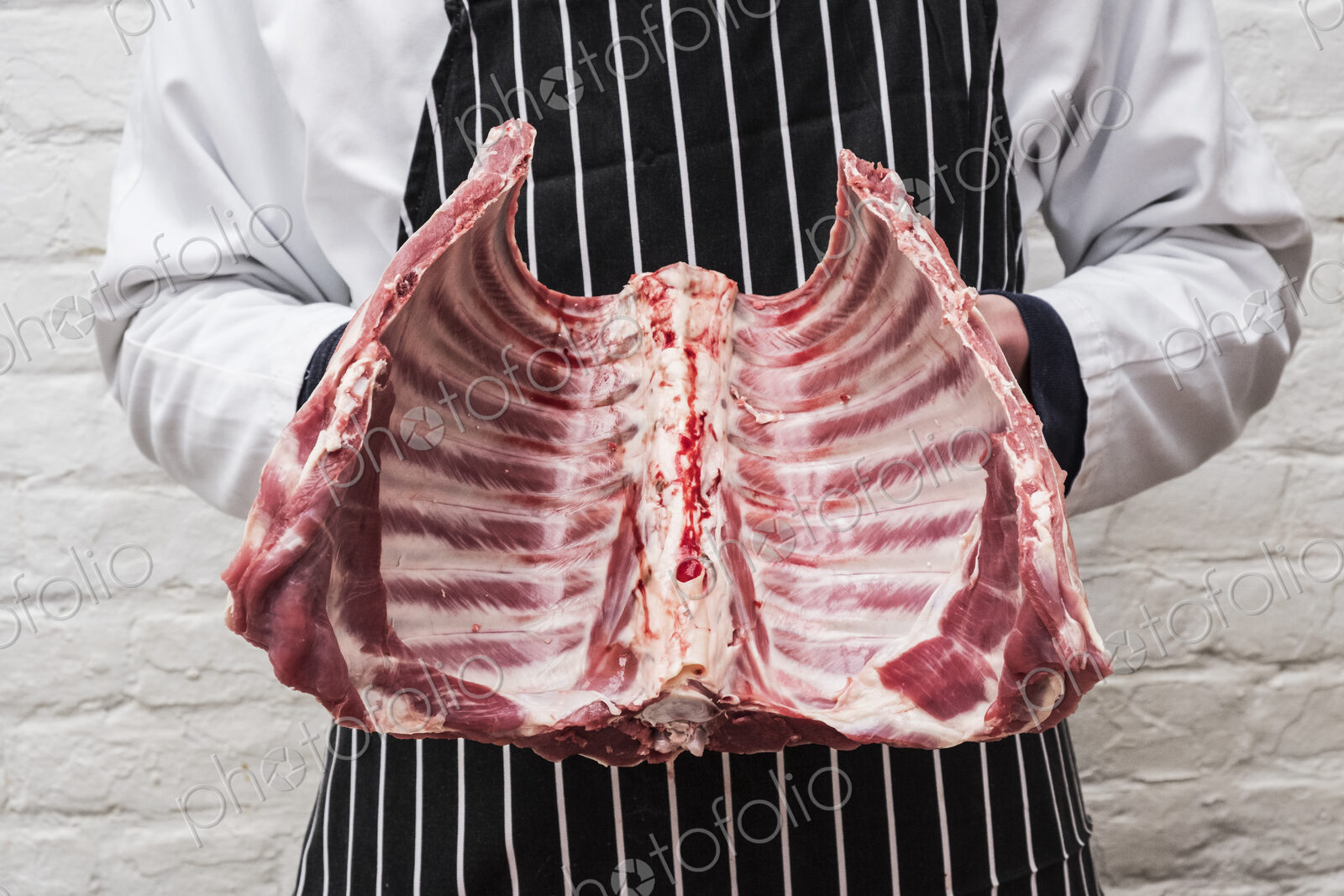 A butcher holding the ribs of a lamb carcass.