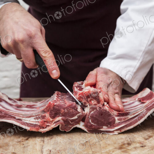 A butcher using a sharp knife to prepare lamb ribs for rack of lamb. A butcher using a sharp knife to prepare lamb ribs for rack of lamb.