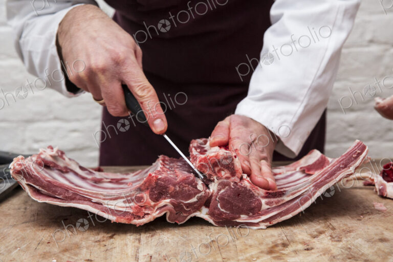 A butcher using a sharp knife to prepare lamb ribs for rack of lamb.