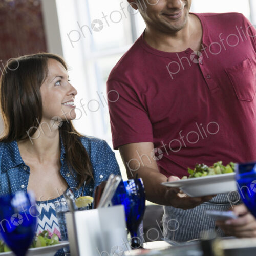 A cafe interior. A man in a waiter's apron serving a meal to two women at a table. A cafe interior. A man in a waiter's apron serving a meal to two women at a table.