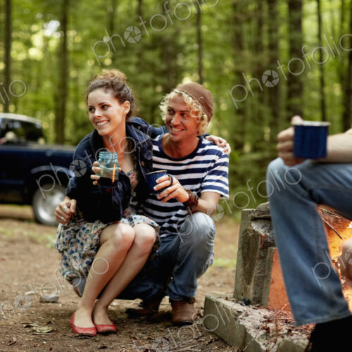 A campsite in the woods. Three people sitting around a campfire at dusk.