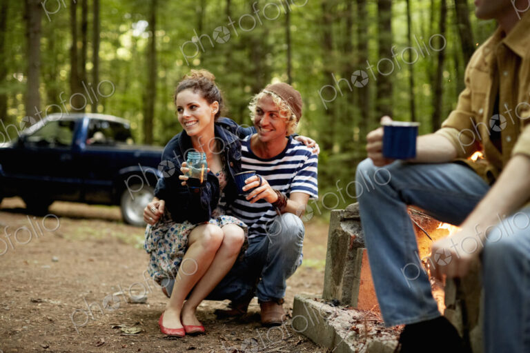 A campsite in the woods. Three people sitting around a campfire at dusk.