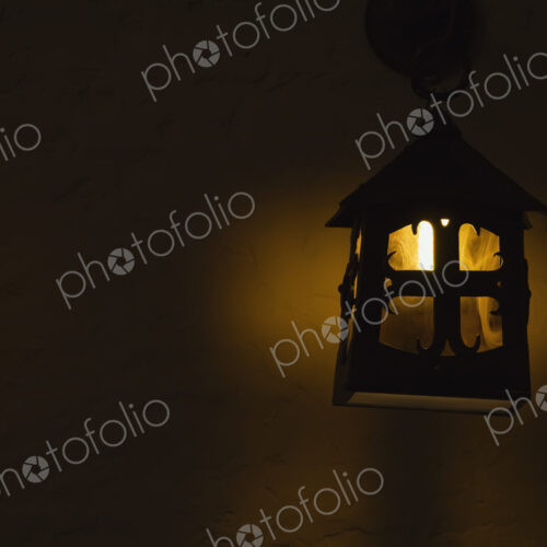 A candle lit in an outdoor lamp on a wall at night. A candle lit in an outdoor lamp on a wall at night.