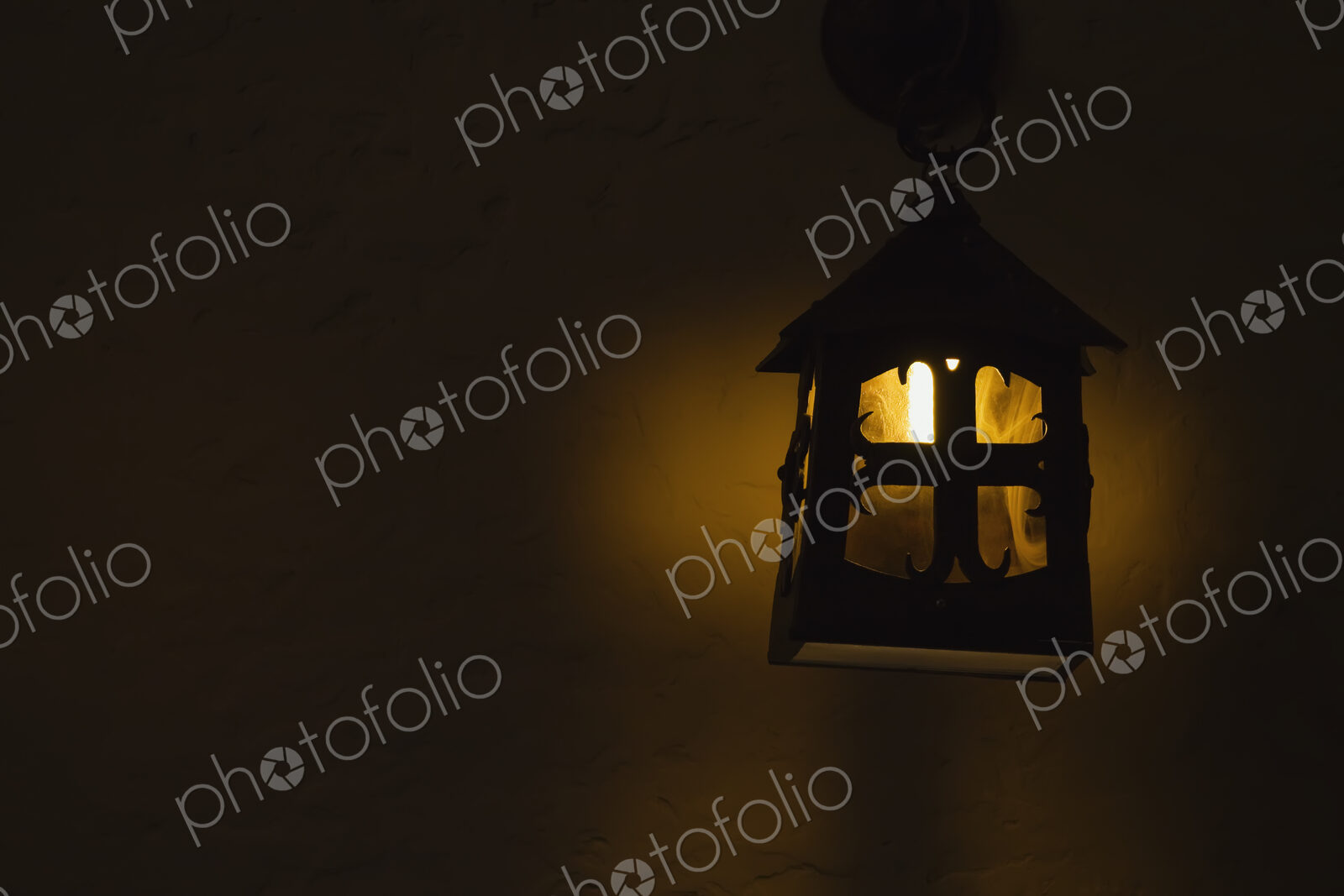 A candle lit in an outdoor lamp on a wall at night.
