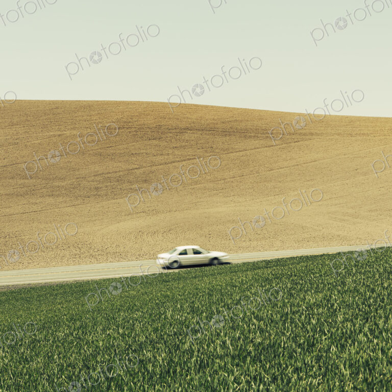 A car driving on am uphill slope, surrounded by farmland and lush, green fields of…