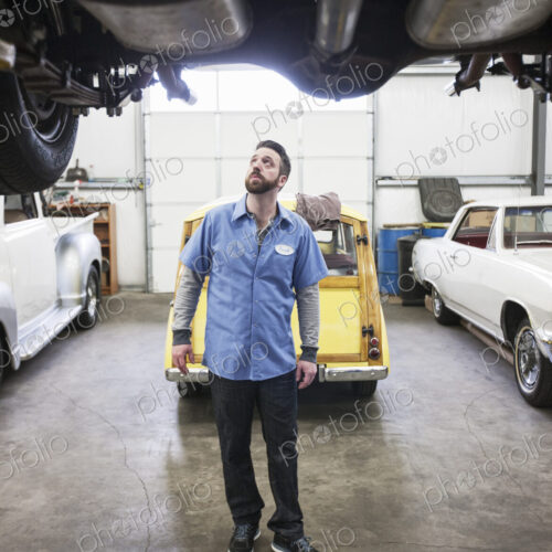 A car mechanic checking the undercarriage of an automobile he's working on in a shop.