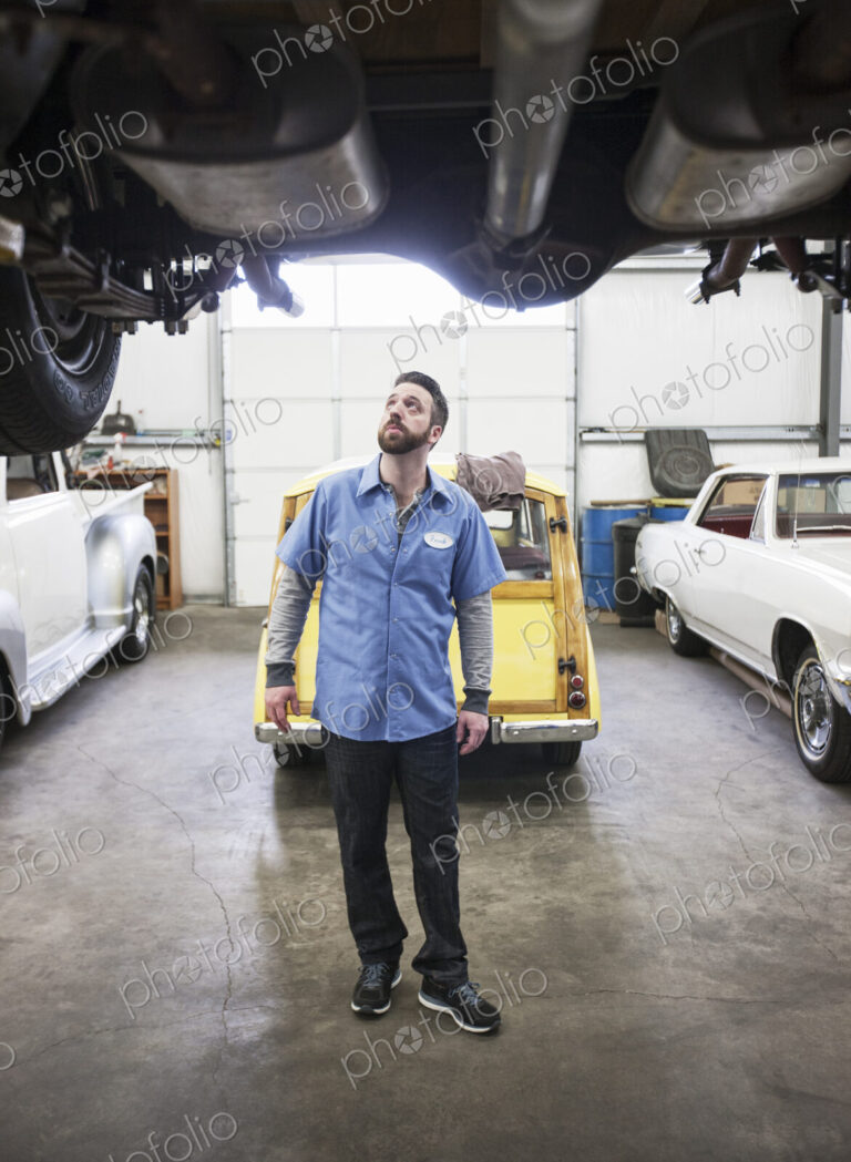 A car mechanic checking the undercarriage of an automobile he's working on in a shop.