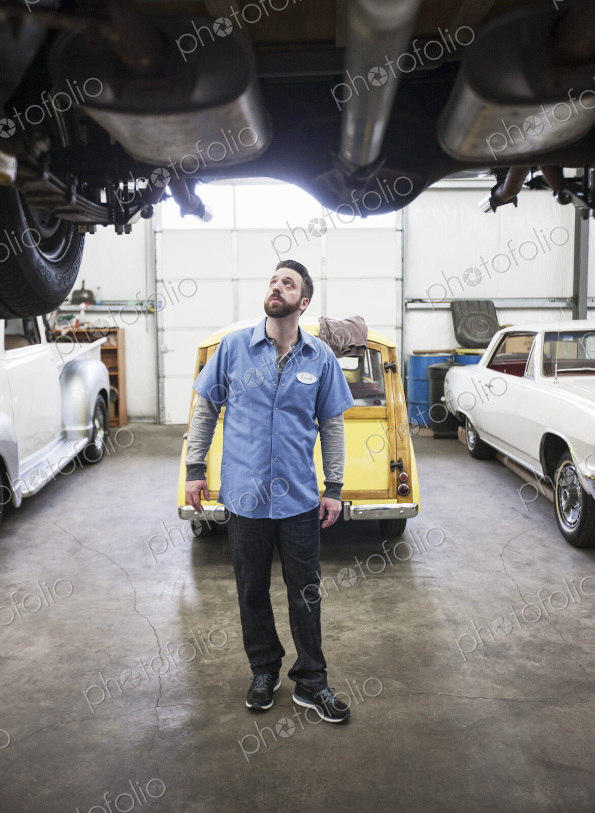A car mechanic checking the undercarriage of an automobile he’s working on in a shop.