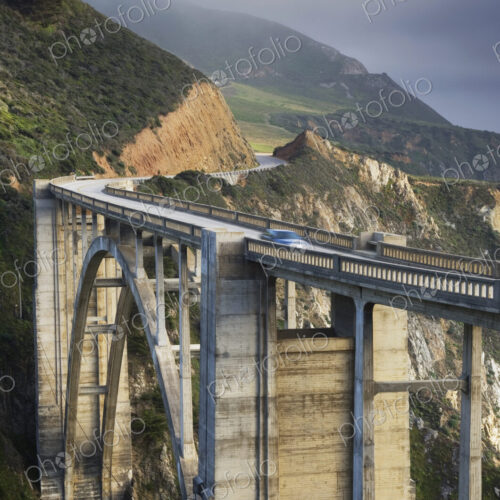A car on a bridge on the Big Sur Pacific coastline, mountains and mist.