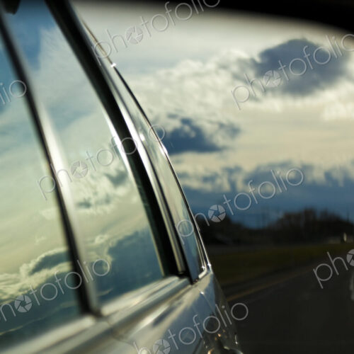 A car side mirror reflection of a road and cars at night, a storm sky, on Highway I-90.