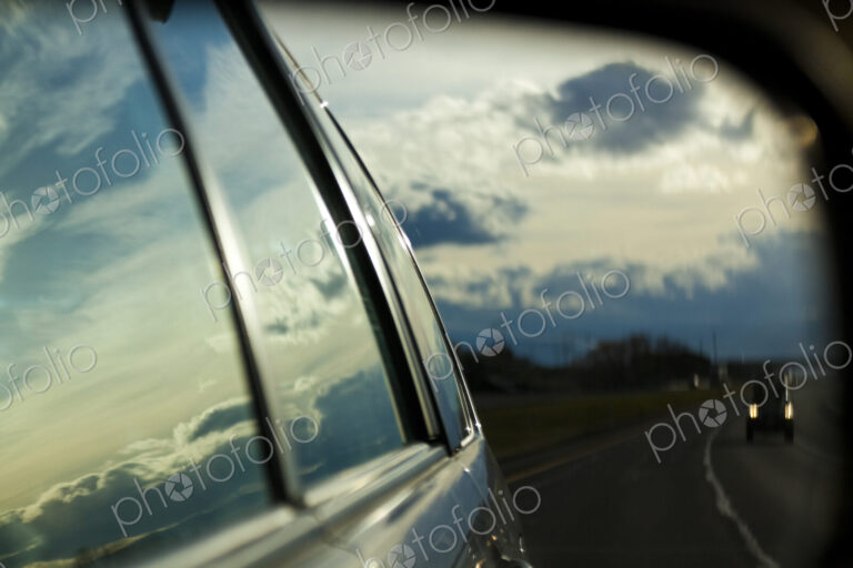 A car side mirror reflection of a road and cars at night, a storm sky, on Highway I-90.