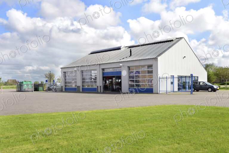 A car workshop or garage with doors open and cars on the forecourt.