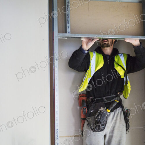 A carpenter in a small space fitting a shelf into a wall cupboard.