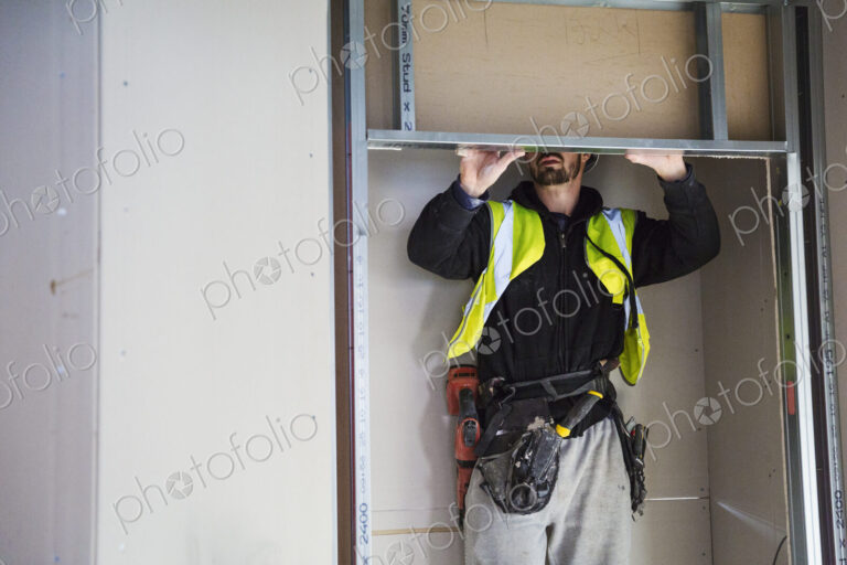 A carpenter in a small space fitting a shelf into a wall cupboard.