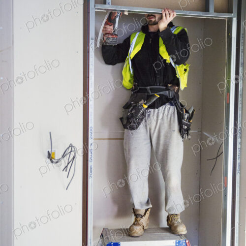 A carpenter in a small space fitting a shelf into a wall cupboard.