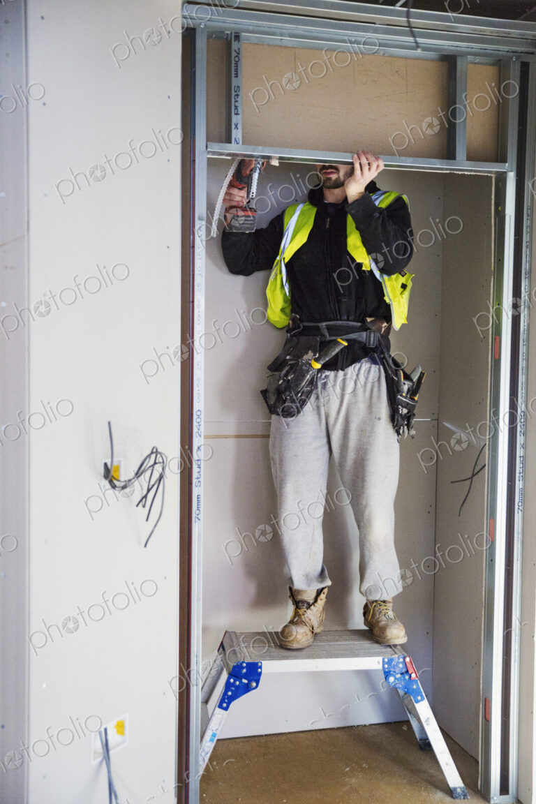 A carpenter in a small space fitting a shelf into a wall cupboard.