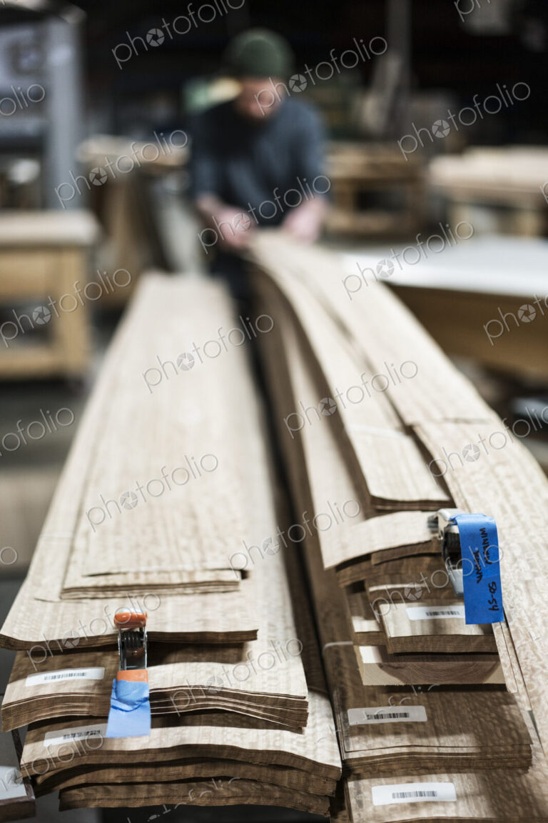 A carpenter in a woodworking shop gathering pieces of wood veneer.
