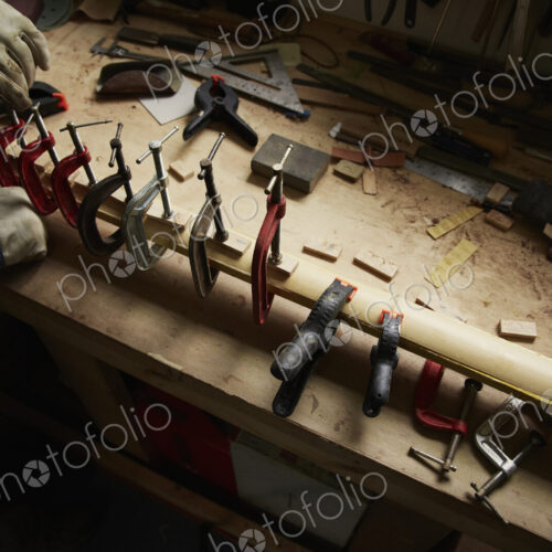 A carpenter wearing protective gloves using clamps on a piece of wood.
