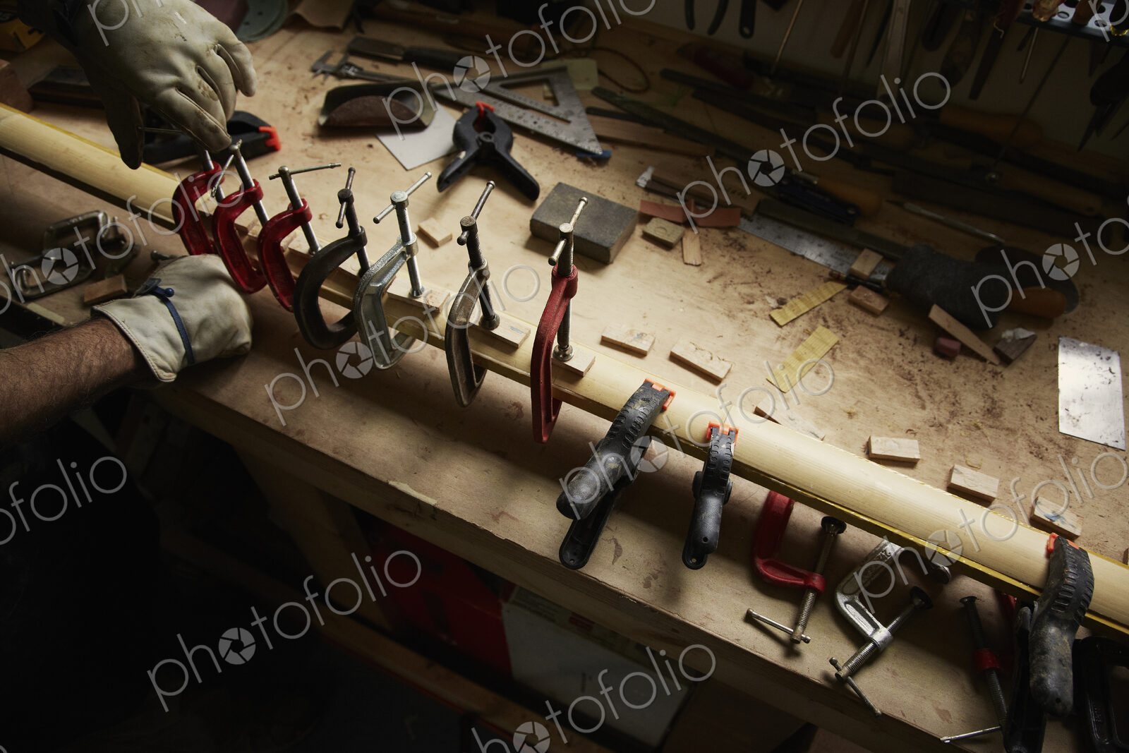A carpenter wearing protective gloves using clamps on a piece of wood.