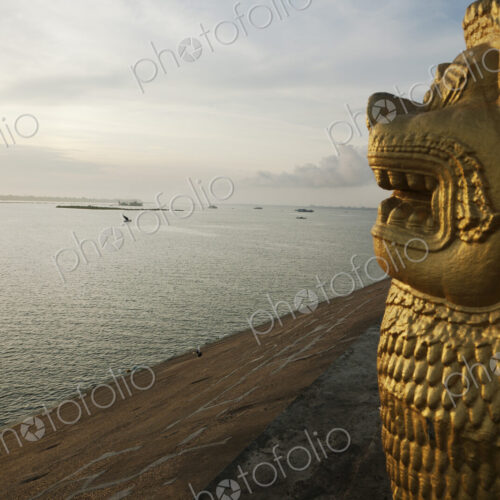 A carved lion head statue in profile overlooking the Tonle Sap River at dawn.