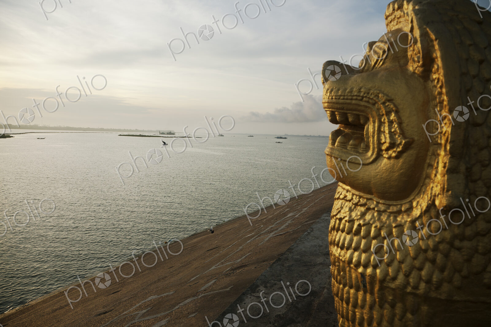 A carved lion head statue in profile overlooking the Tonle Sap River at dawn.