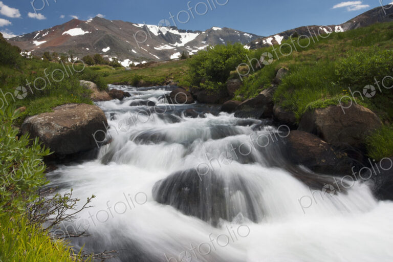 A cascade of fast flowing white water over rocks in a valley in the mountains.