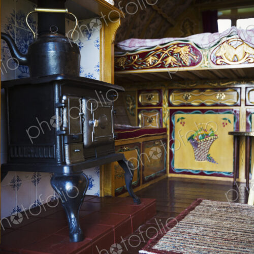 A cast iron stove with large metal kettle, a mantlepiece and storage cupboards and… A cast iron stove with large metal kettle, a mantlepiece and storage cupboards and…
