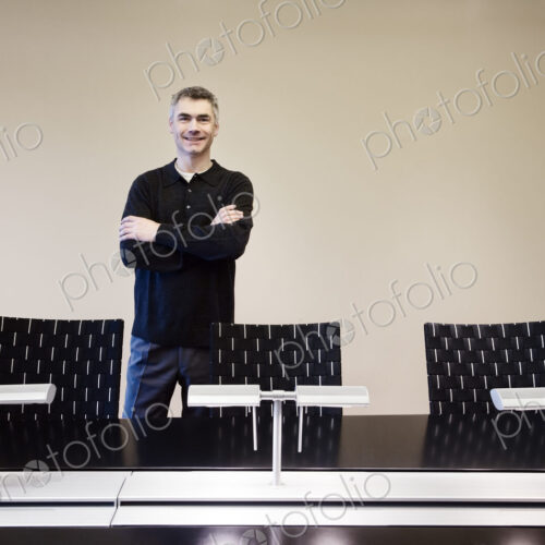 A casually dressed caucasian businessman standing behind an large office conference table.