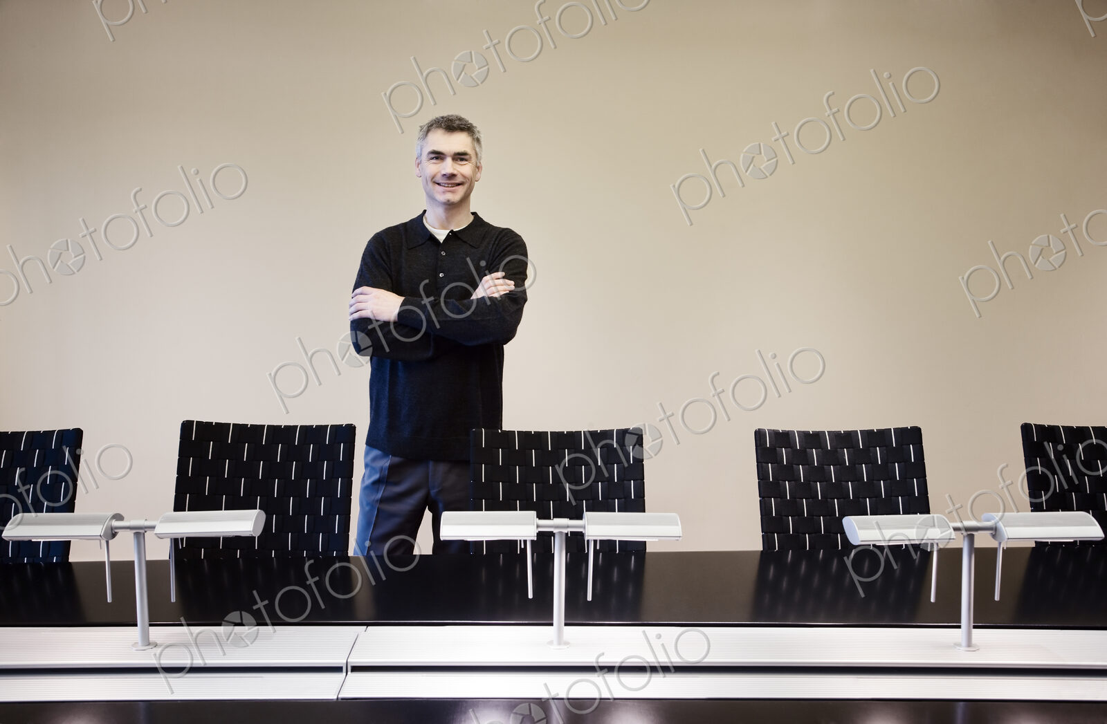 A casually dressed caucasian businessman standing behind an large office conference table.