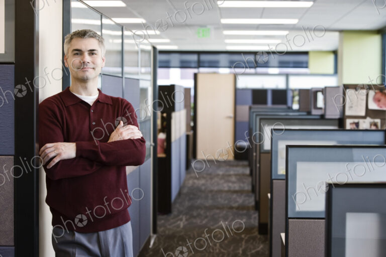 A casually dressed caucasian businessman standing next to his office in a room full of…