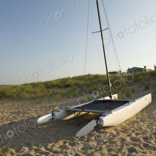 A catamaran sailing boat on the sand, on a beach, with houses in the distance. A catamaran sailing boat on the sand, on a beach, with houses in the distance.