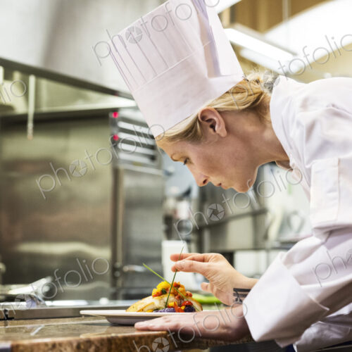 A caucaisan female chef putting the finishing touches on a plate of fish in a… A caucaisan female chef putting the finishing touches on a plate of fish in a…