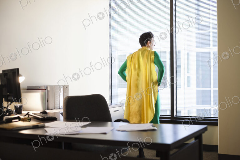 A caucasian businessman office super hero stands at his office window and ponders his…