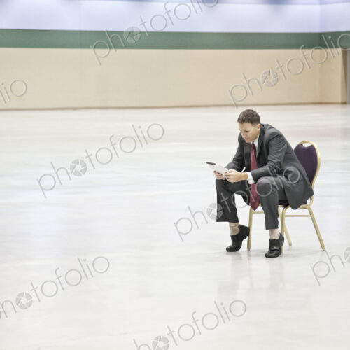 A caucasian businessman texting while sitting in a chair in the middle of a convention…