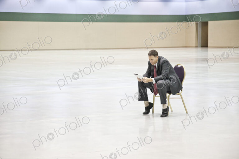 A caucasian businessman texting while sitting in a chair in the middle of a convention…
