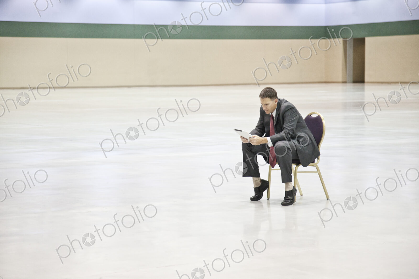 A caucasian businessman texting while sitting in a chair in the middle of a convention…