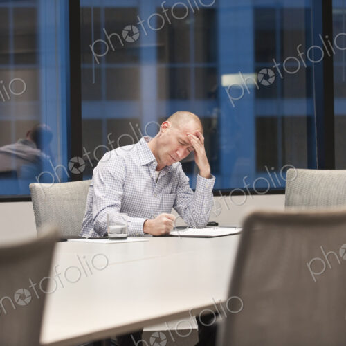 A caucasian businessman under stress while working at night at a conference table. A caucasian businessman under stress while working at night at a conference table.