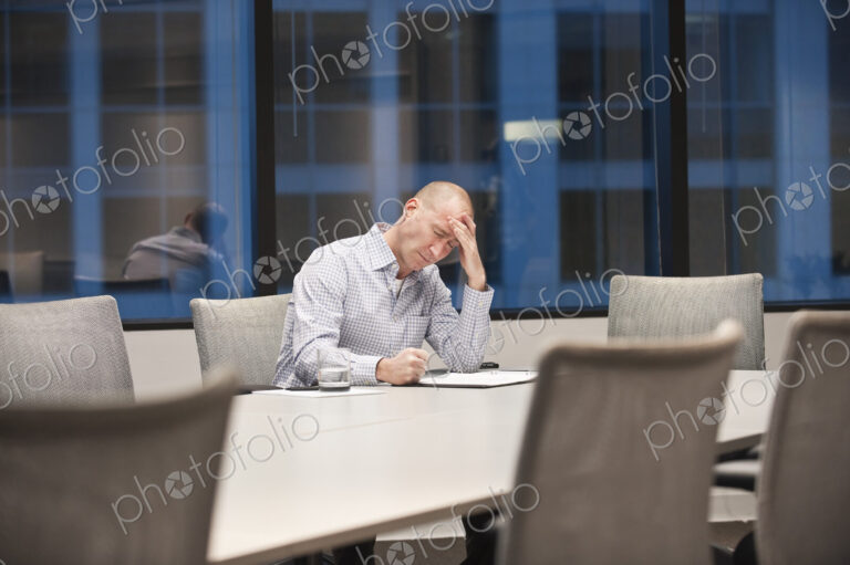 A caucasian businessman under stress while working at night at a conference table.