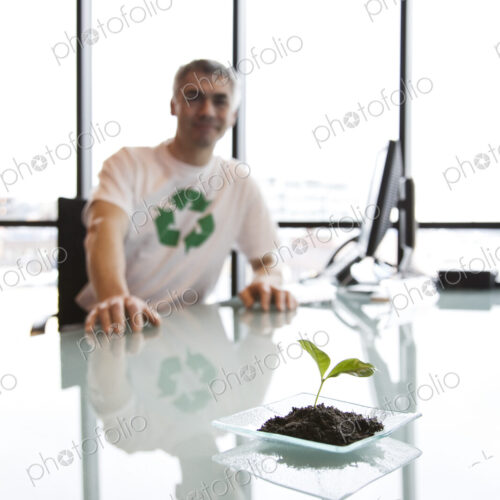 A caucasian businessman wearing a recycle t shirt while sitting at his office desk in… A caucasian businessman wearing a recycle t shirt while sitting at his office desk in…