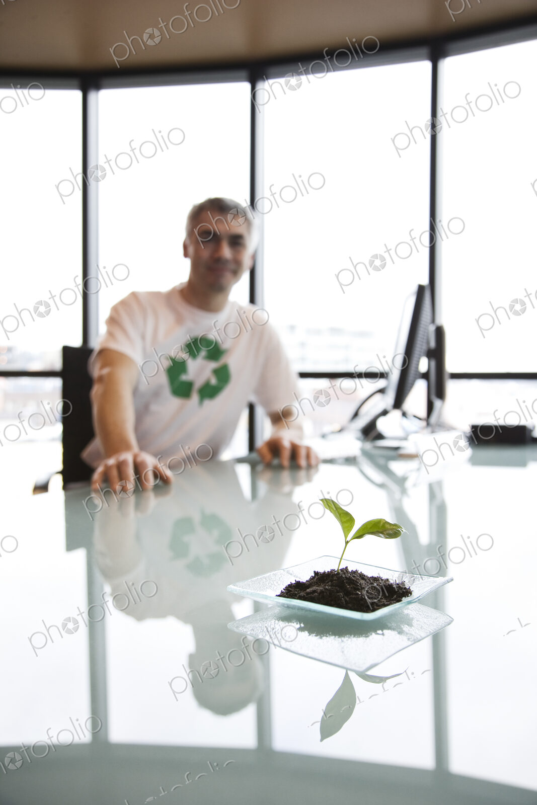 A caucasian businessman wearing a recycle t shirt while sitting at his office desk in…