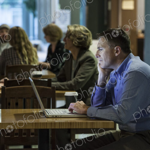 A caucasian businessman working on a laptop computer while sitting in a cafe.